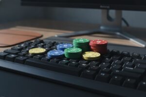 A close-up, slightly elevated perspective of a modern, minimalist keyboard. Scattered across its dark, matte keys are several generic, brightly colored gambling chips in various denominations. Some chips are stacked in small piles, while others lie individually, catching subtle reflections from an unseen light source. The composition emphasizes the interplay between the tangible elements of chance and the digital interface, conveying a mood of focused engagement and potential outcomes. The background is softly blurred, keeping the viewer's attention on the keyboard and chips.