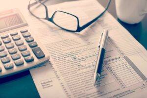 Photo of a calculator, glasses, a financial sheet and a pen.