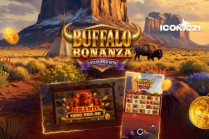 A promotional graphic for the online slot game ‘Buffalo Bonanza Hold and Win’ by ICONIC21. The background depicts a sweeping Western desert landscape at sunset, featuring large mesas, a tipi on the left, and a buffalo grazing on the right. The game’s title is presented in the centre in bold 3D gold lettering with large buffalo horns and a purple ‘HOLD AND WIN’ ribbon. Glowing gold coins float across the scene, and the ICONIC21 logo is located in the top-right corner.