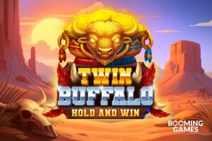 Here is the British English Alt Text for this promotional image: **Alt Text:** Promotional artwork for the 'Twin Buffalo Hold and Win' game by Booming Games. The central graphic features a golden buffalo head emblem sitting atop a pot of coins, positioned above the stylised game title. The background depicts a desert canyon landscape at sunset with a buffalo skull in the foreground.