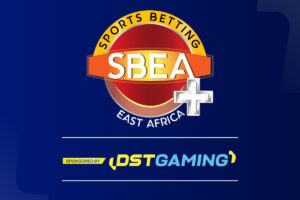 A promotional banner for the Sports Betting East Africa (SBEA+) event on a dark blue background. The central circular logo features a red globe, a yellow arch reading ‘SPORTS BETTING’, and an orange banner with the letters ‘SBEA’ next to a large white plus sign. The bottom of the image includes a ‘SPONSORED BY’ section with the DSTGAMING logo in yellow and blue.