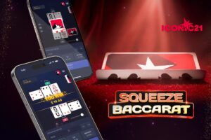 A promotional graphic for ICONIC21’s ‘Squeeze Baccarat’. The image shows two smartphones displaying the game’s mobile interface, with one showing a ‘YOU WIN’ notification. In the background, a physical playing card is placed on a red velvet surface, with its edges curled up to simulate a ‘squeeze’ under a spotlight. The ICONIC21 logo appears in the top-right corner.