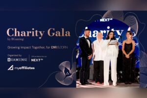 A promotional event graphic. The left half displays text in a gold font reading ‘Charity Gala by BGaming’, followed by the tagline ‘Growing Impact Together, for DAR BJORN’. Below this, event partner details are listed: ‘Organised by BGAMING’, ‘Official Media Partner NEXT.io’, and the white logo for ‘myaffiliates’. The right half contains a photograph of four people on a stage framed by a circular cutout.
