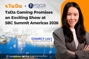 A promotional industry graphic with a light, subtly patterned grey background on the top-left and a large orange section on the right. In the upper-left corner, text reads ‘TaDa x FOCUS GAMING NEWS’ alongside their respective logos, followed by the main headline: ‘TaDa Gaming Promises an Exciting Show at SBC Summit Americas 2026’ in bold black lettering. On the right side, a portrait features Charcy Liu, Director of Marketing, smiling with arms crossed and wearing a grey blazer over a white top.